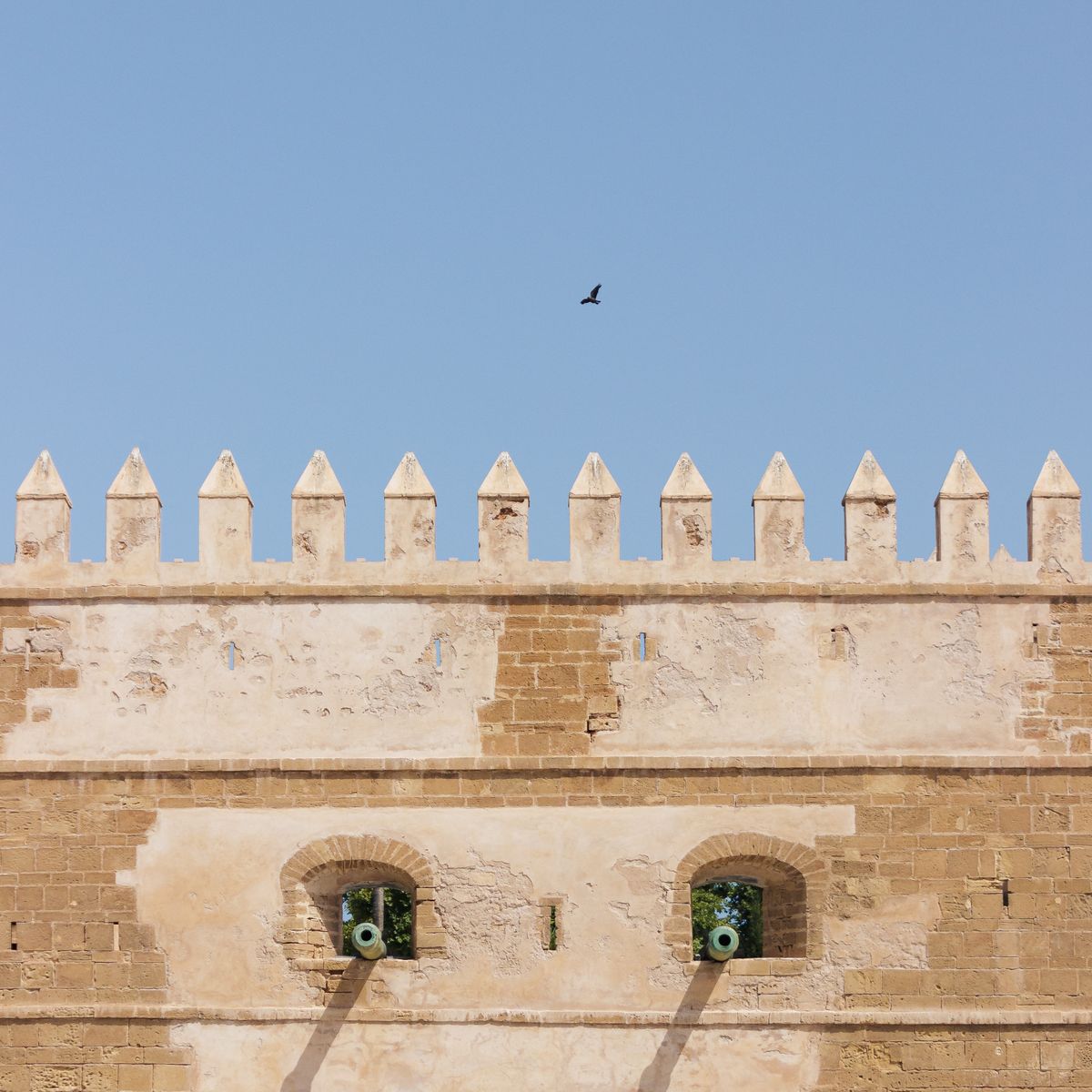 Mur de forteresse en pierre avec créneaux se détachant sur un ciel bleu, fortification bastionnée