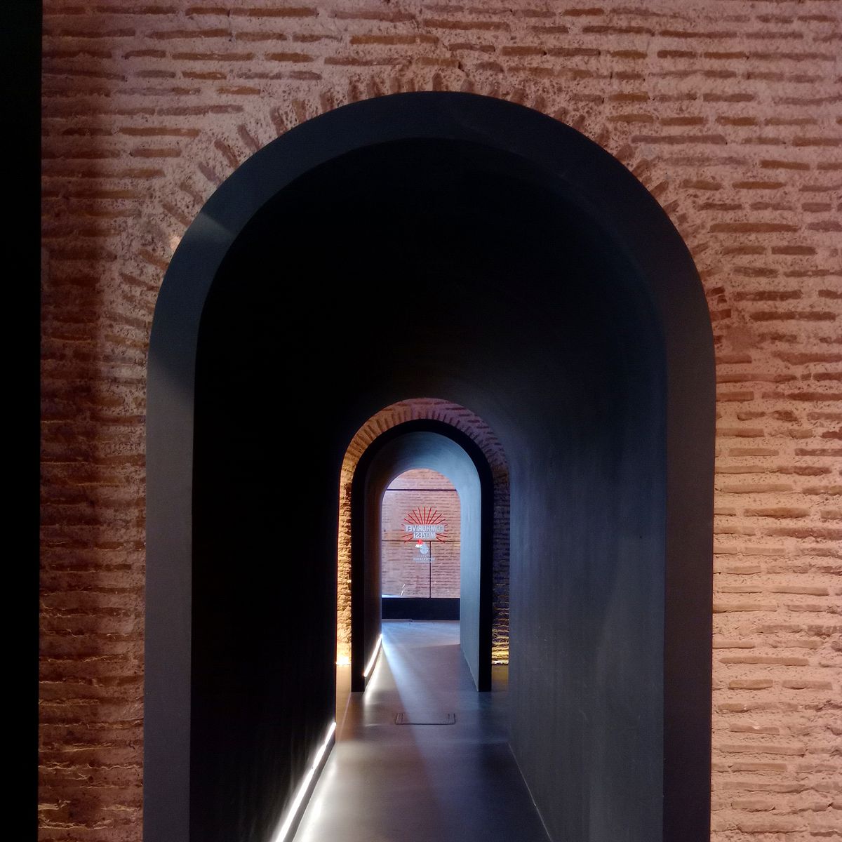 Couloir voûté en briques éclairé, jeux de lumière et d'ombres sous la voûte de pierre