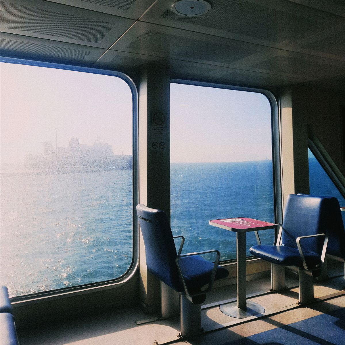 Intérieur d'un bateau avec grandes vitres sur la mer, deux sièges bleus et table